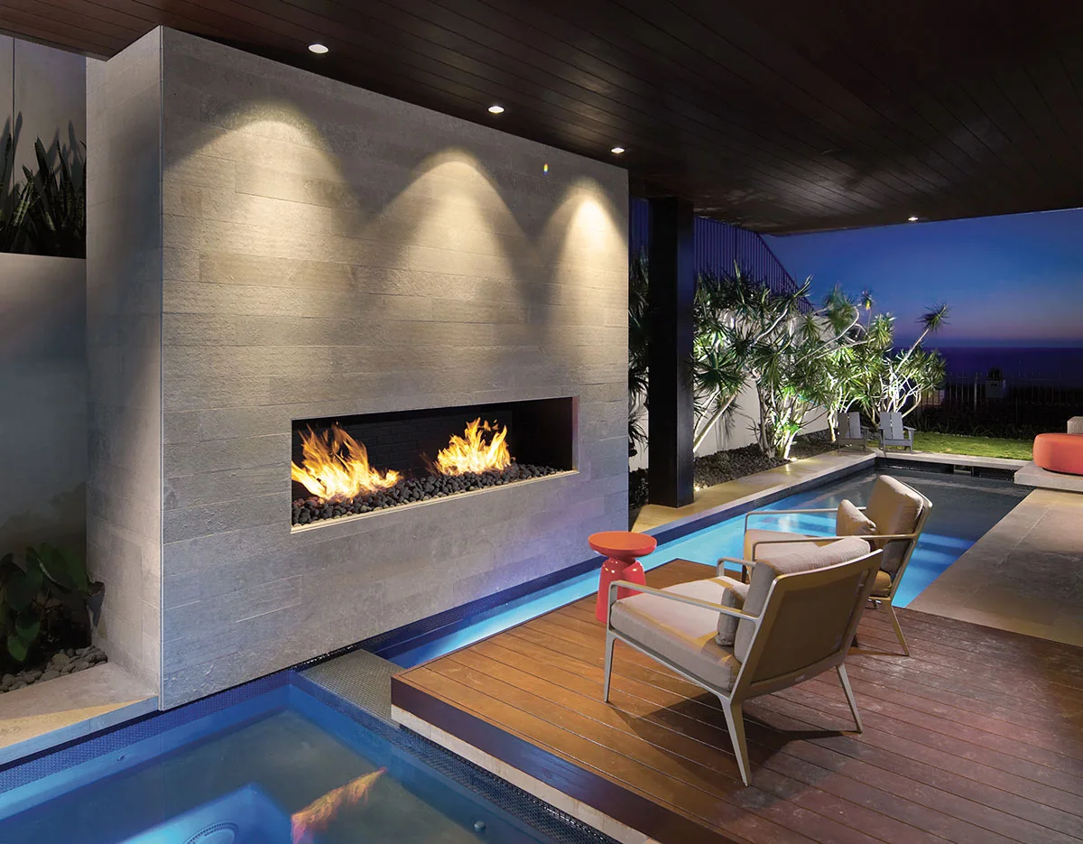 Covered outdoor lounge with a fireplace and blue illuminated water feature
