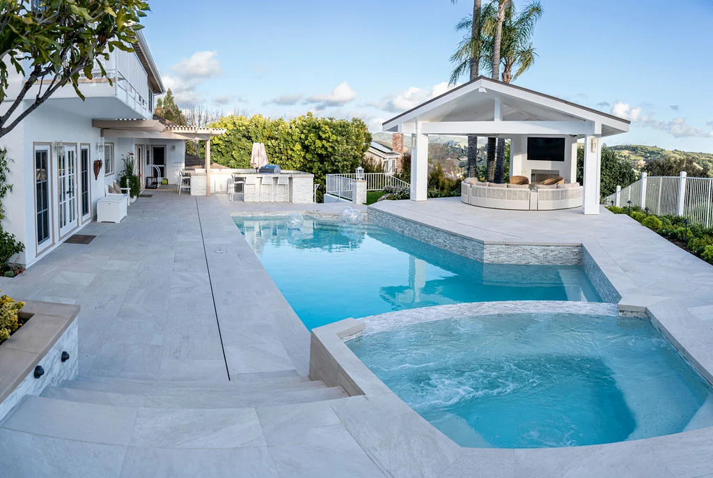 Light stone pool terrace overlooking a white outdoor pavilion