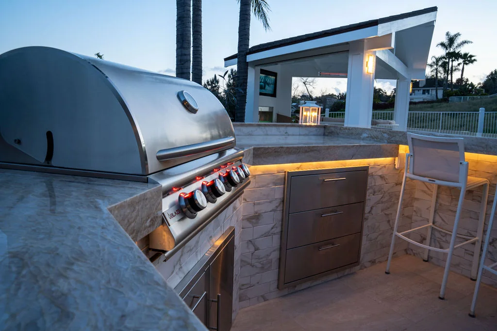 Built-in stainless steel grill and outdoor kitchen beside a pool