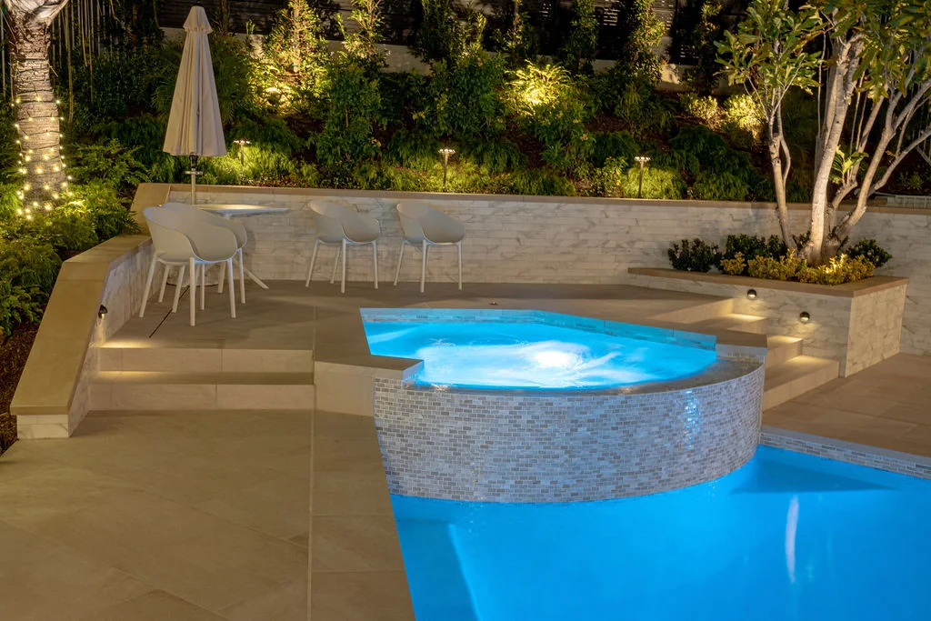 Illuminated pool and raised spa framed by a stone retaining wall