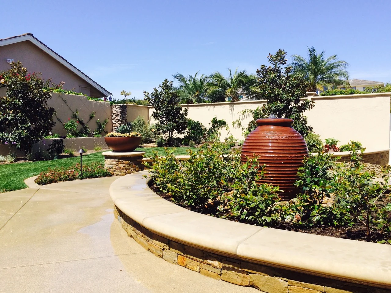 Curving raised planter with colorful flowers and a large terracotta vessel