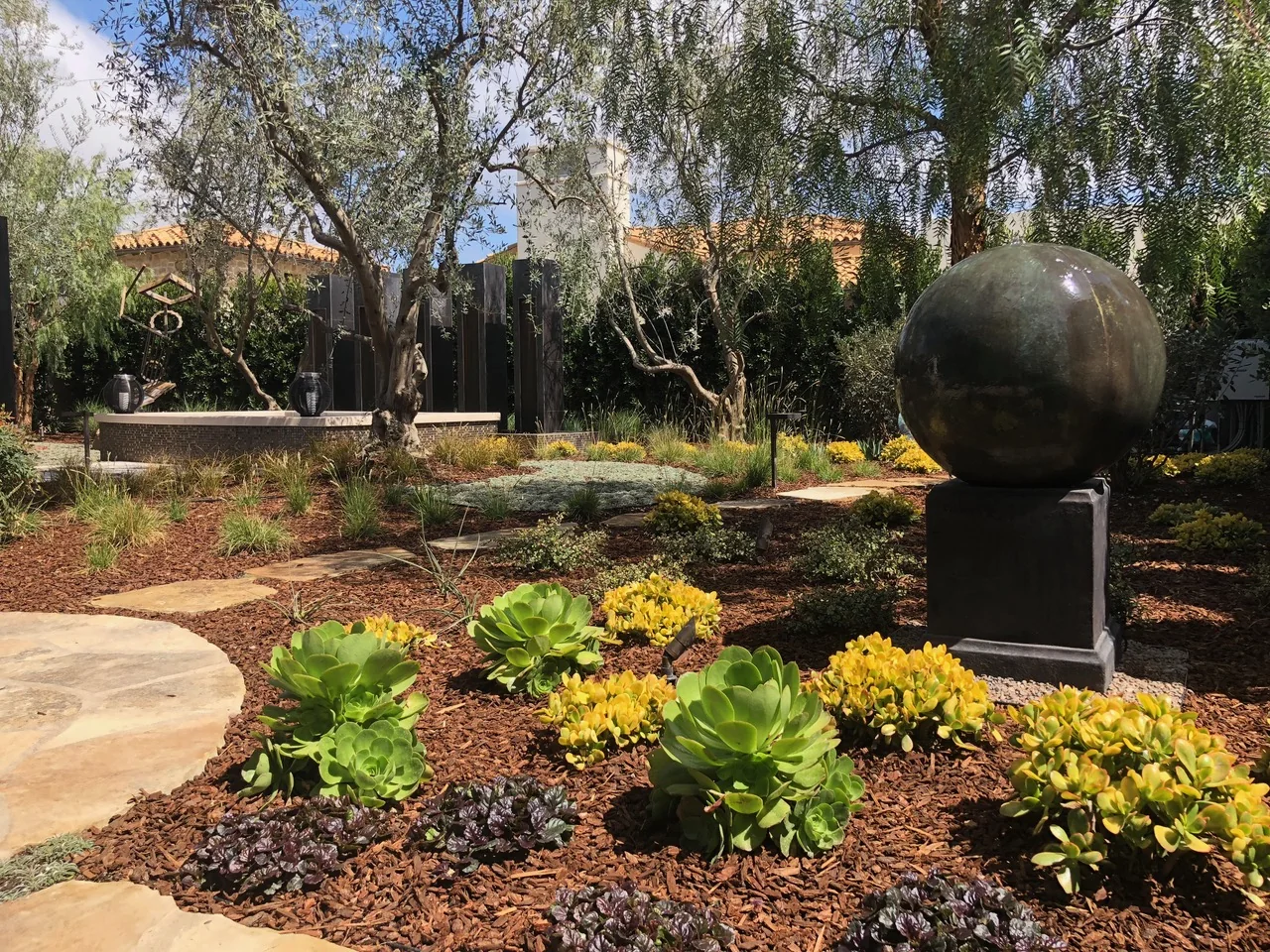 Water sphere sculpture in a garden with flowers and stone paving