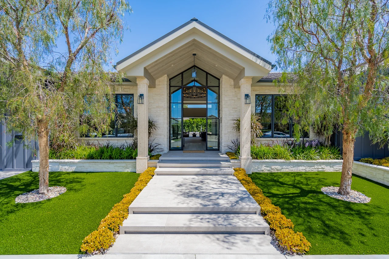 Straight stone pathway framed by lawn, flowering borders, and trees