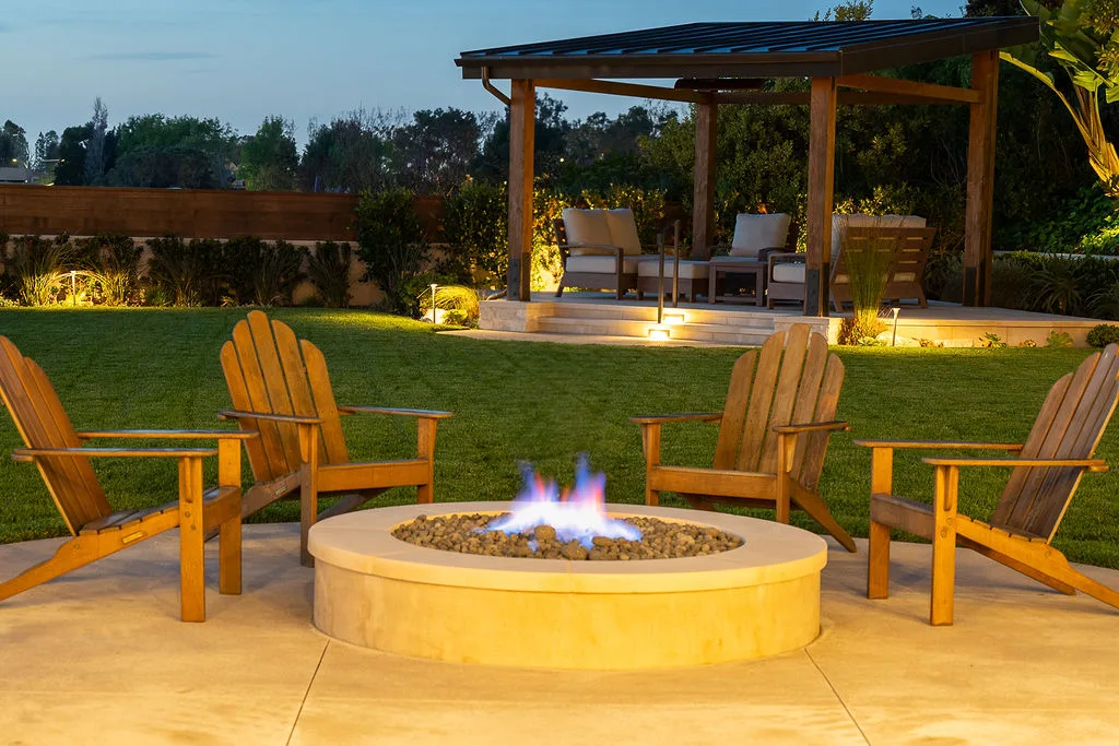 Circular garden fire pit with timber chairs and a pergola beyond